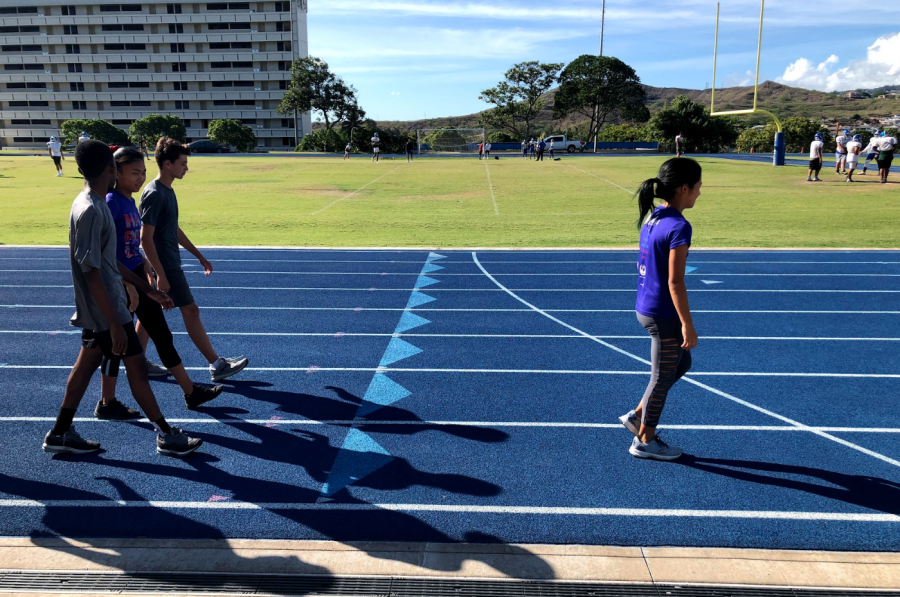 The Cross Country team warms up on the track field with the sun shining. 