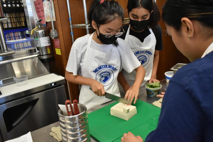 Miley Chun cuts the block of tofu into cubes while Khrista Kaina watches.