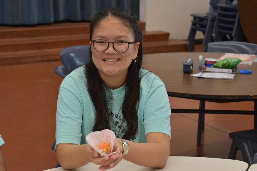 Sydney Tom (11) shows off one of the different kinds of paper flowers students could make at the French language booth in the cafeteria.